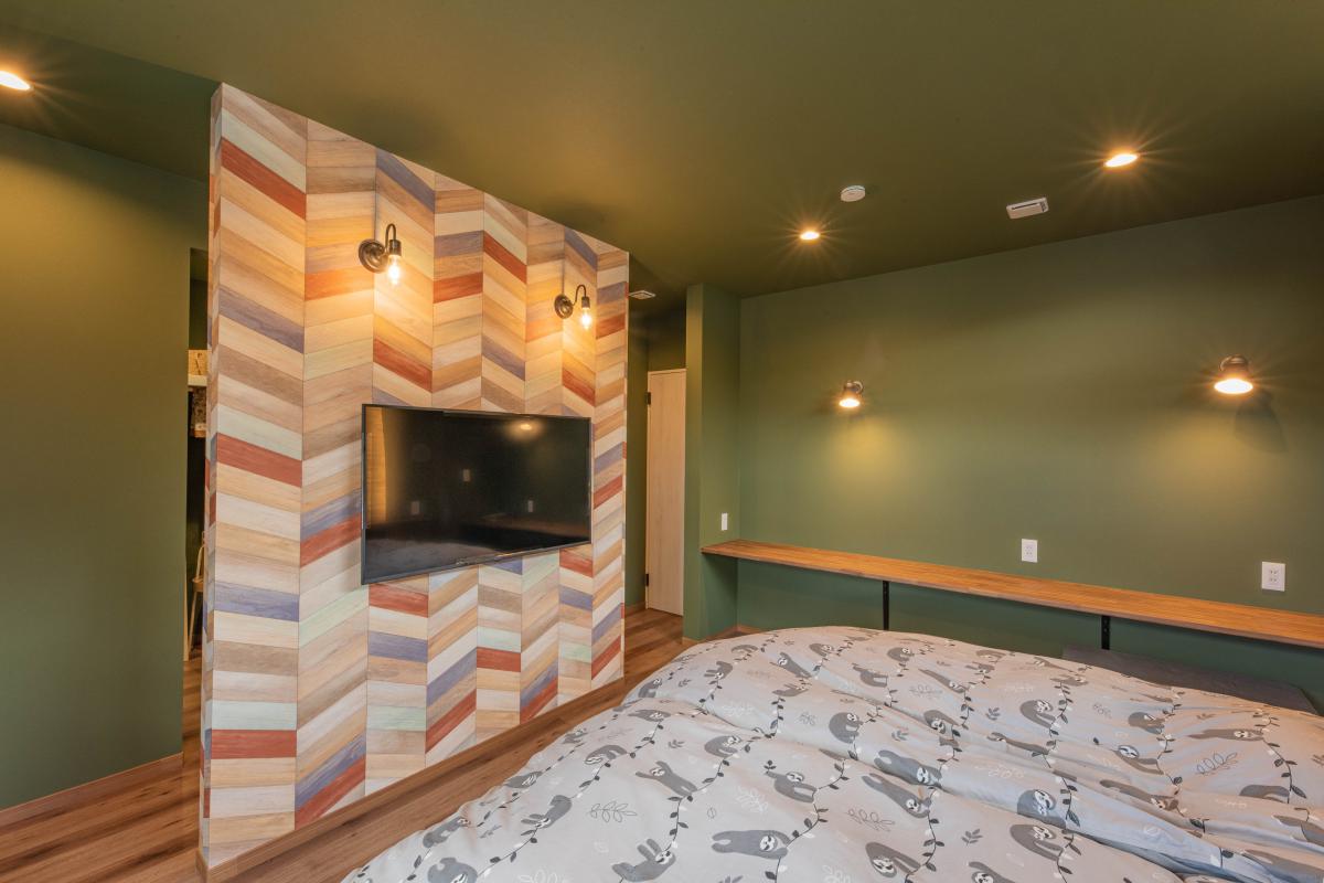 部屋全体を癒し効果もある深いグリーンでまとめられた寝室は、カラフルなヘリンボーンの壁紙が目を引きます。